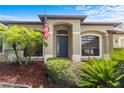 Exterior shot showcasing the front entrance with a blue door, beautiful plants, and an American flag at 8836 Alafia Cove Dr, Riverview, FL 33569