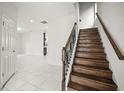 Open entryway with a staircase featuring wood steps and a dark metal railing, plus tile flooring throughout at 13299 Wildgrass Trl, Odessa, FL 33556
