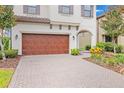 Close-up of a two-car garage and front exterior of a home with manicured landscaping and paver driveway at 13299 Wildgrass Trl, Odessa, FL 33556