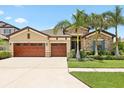 Beautifully landscaped home with a three-car garage and mature palm trees on a sunny day at 14514 Woodland Spur Dr, Lithia, FL 33547