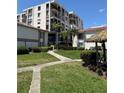Exterior of a condo community with mature palm trees, a tiki hut, and sidewalk access at 6218 Palma Del Mar # 303, St Petersburg, FL 33715