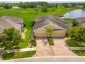 Aerial view of the tan-colored home featuring a red brick driveway, well-kept landscaping, and pond views at 644 Chipper Dr, Sun City Center, FL 33573