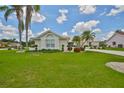 This is an eye-level shot showcasing lush green grass, palm trees, and tasteful landscaping that frame a well-maintained beige house at 602 Deep Lake Ln, Sun City Center, FL 33573