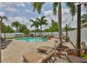 This backyard features a sparkling pool surrounded by palm trees, lounge chairs, and travertine tile at 13728 Artesa Bell Dr, Riverview, FL 33579