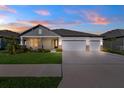 Single-story home featuring a three-car garage and a well-manicured lawn, captured during a vivid sunset at 8840 Mugnai St, Riverview, FL 33578