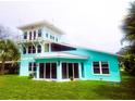 Beautiful turquoise home with floor-to-ceiling glass doors, a charming tower, and a lush green yard at 1626 Sea Breeze Dr, Tarpon Springs, FL 34689