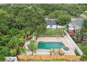 Aerial view of a backyard oasis with a large pool, a spa, palm trees, white gravel, a wood fence and lush greenery at 6 N Orion Ave, Clearwater, FL 33765