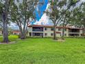 Expansive green lawn surrounded by mature trees and the residential building with screened balconies on a bright day at 5785 Gardens Dr, Sarasota, FL 34243