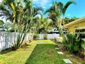 Serene backyard featuring lush greenery, mature palm trees, a stone paver walkway, and white vinyl privacy fence at 2645 Woodring Dr, Clearwater, FL 33759