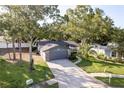 Wide aerial view of a one-story home featuring a gray garage, stone accents, and a well-manicured lawn with a palm tree at 399 Walnut Ct, Palm Harbor, FL 34683