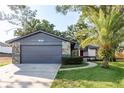 Charming one-story home featuring a gray garage, stone accents and a well-manicured lawn with a vibrant palm tree at 399 Walnut Ct, Palm Harbor, FL 34683