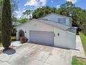 Two-car garage with gray door, exterior wall extension and landscaped yard with a beautiful, mature cypress tree at 15722 Gardenside Ln, Tampa, FL 33624