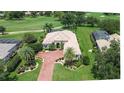 Aerial view of a tile roof house featuring a red brick driveway, a manicured lawn, palm trees, and a golf course view at 12713 Grand Traverse Dr, Dade City, FL 33525