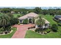 Aerial shot of a beautifully landscaped home with a red brick driveway, manicured lawn, and tropical palm trees at 12713 Grand Traverse Dr, Dade City, FL 33525