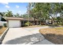 Inviting single-story home with a long driveway, attached garage, and a lush green lawn surrounded by mature trees at 3907 W Azeele St, Tampa, FL 33609