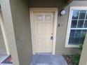 Beige front door for unit 102, with a doorbell, peep hole, and an outdoor light fixture at 36137 Lake Chase Blvd # 102, Zephyrhills, FL 33541
