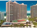 Exterior of a beachfront condominium featuring a tennis court, palm trees, and a parking area at 1340 Gulf Blvd # 12A, Clearwater Beach, FL 33767