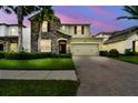 Charming home featuring a stone facade, well-manicured lawn, and a brick paved driveway leading to a two-car garage at dusk at 4544 Vermillion Sky Dr, Wesley Chapel, FL 33544