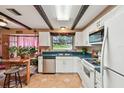 Bright eat-in kitchen features white cabinets, modern appliances, dark wood beams, and tile floors at 855 Pinewood W Ter, Palm Harbor, FL 34683