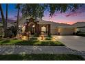 Inviting home exterior with stone accents, a three-car garage, and an illuminated, landscaped yard at dusk at 8704 Winsome Way, Land O Lakes, FL 34637