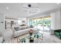 Bright living room featuring modern circular lighting fixture, large windows, and sliding glass doors to the backyard at 32203 Mahogany Valley Dr, Wesley Chapel, FL 33543