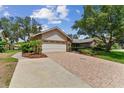 Paver driveway and two car garage of charming single-story home surrounded by lush landscaping and mature trees at 1810 Tamerlane Pl, Brandon, FL 33510