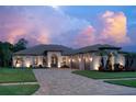 Charming single-story home at dusk, featuring a paver driveway, lush landscaping, and a three-car garage at 16304 Wild Mallard Dr, Odessa, FL 33556