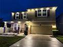 Night view of home's exterior with warm lighting, landscaped yard, two-car garage and covered front porch at 3052 Living Coral Dr, Odessa, FL 33556