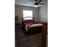 Comfortable bedroom with wood-look floors, ceiling fan, and a cozy bed with warm red linens at 702 Cypress Pl, Sun City Center, FL 33573