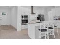 Bright kitchen featuring modern appliances, white cabinets, an island with seating, and wood flooring at 17415 Holly Well Ave, Wimauma, FL 33598
