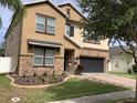 Charming two-story tan home with manicured front yard, a two-car garage, and stacked stone details at 2588 Bartolo Dr, Land O Lakes, FL 34639