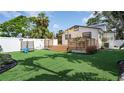 Well-maintained backyard with artificial turf, a wooden deck, white fencing, and mature tropical landscaping at 500 62Nd S St, St Petersburg, FL 33707
