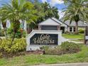A neighborhood sign with lush landscaping reads 'Lake Valencia East' with a home in the background at 5110 Lake Valencia E Blvd, Palm Harbor, FL 34684