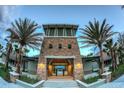 Beautiful clubhouse entrance featuring stone accents, palm trees, and a glimpse of a water view through the gate at 31980 Goddard Dr, Wesley Chapel, FL 33543