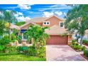 Two-story tan home with a tile roof, brick driveway, manicured lawn, and a two-car garage at 9883 Sago Point Dr, Seminole, FL 33777