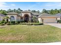 Tan single-story house with a red door and lush landscaping at 5378 Legend Hills Ln, Spring Hill, FL 34609