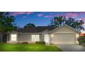 Tan one-story house with a two-car garage, landscaped lawn, and evening lighting at 4336 Lightfoot St, Spring Hill, FL 34609