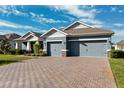 Two-story home with gray exterior, three car garage, and a brick driveway at 19907 Tattnall Way, Brooksville, FL 34601