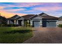 Two-story home with gray exterior, three car garage, and a brick driveway at dusk at 19907 Tattnall Way, Brooksville, FL 34601