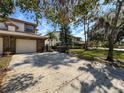 Townhouse exterior featuring a two-car garage, brick accents, tile roof, and mature landscaping at 1203 Clays Trl # 406, Oldsmar, FL 34677