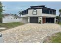 Two story modern home featuring dark metal roof, block driveway, stucco siding, and single garage door at 1616 Sea Breeze Dr, Tarpon Springs, FL 34689