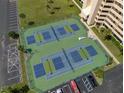 Aerial view of tennis courts with vibrant blue and green surfaces, nestled next to condos and parking at 5915 Sea Ranch Dr # 211, Hudson, FL 34667