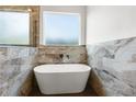 Elegant bathroom with a standalone tub, marble tile, and modern fixtures beneath a bright window at 16043 Penn State Rd, Weeki Wachee, FL 34614