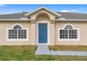 Close-up of a home's entrance featuring a blue front door flanked by arched windows and fresh landscaping at 1313 Gatewood Ave, Spring Hill, FL 34608