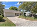 Quaint single-story home featuring brick driveway, attached garage, and manicured front lawn at 6530 Pine Meadows Dr, Spring Hill, FL 34606