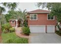 Red brick home featuring an attached garage and a beautifully landscaped front yard with tropical plants at 1218 Castle Ter, Tarpon Springs, FL 34689