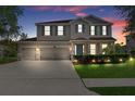Inviting two-story home at dusk featuring a three-car garage, manicured lawn and charming curb appeal at 13619 Hunters Point St, Spring Hill, FL 34609