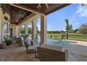 Covered outdoor patio featuring ceiling fans, travertine tile and a serene view of the pool and golf course at 3026 Wentworth Way, Tarpon Springs, FL 34688