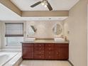 Bathroom with dual sinks, cherry-tone cabinets, a tiled backsplash, and a large garden tub under a window at 5411 Joyner Ave, Spring Hill, FL 34608