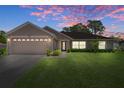Charming single-story home with an attached two-car garage, lush green lawn, and beautiful sunset at 11310 Limpkin Rd, Weeki Wachee, FL 34614